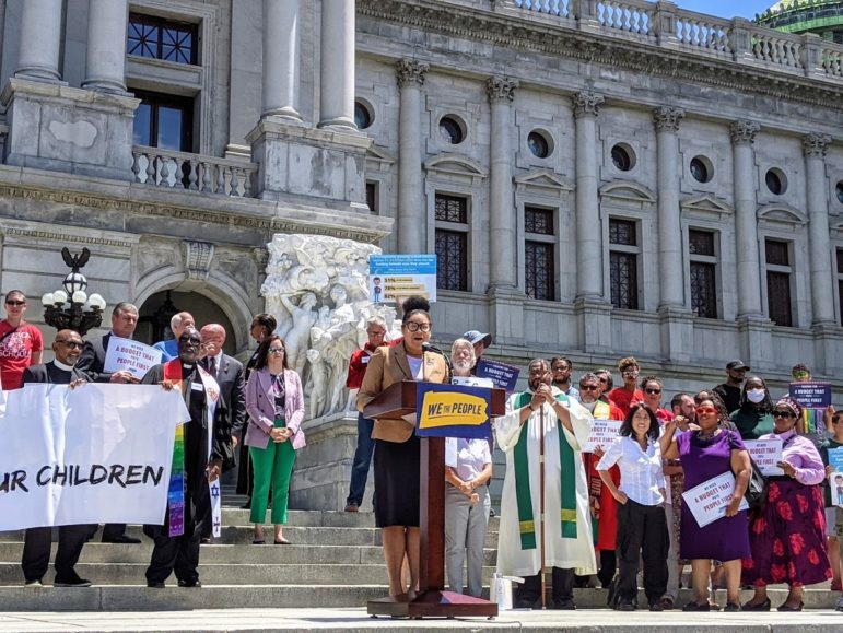 Multiple people stand outside promoting economic prosperity and social justice.